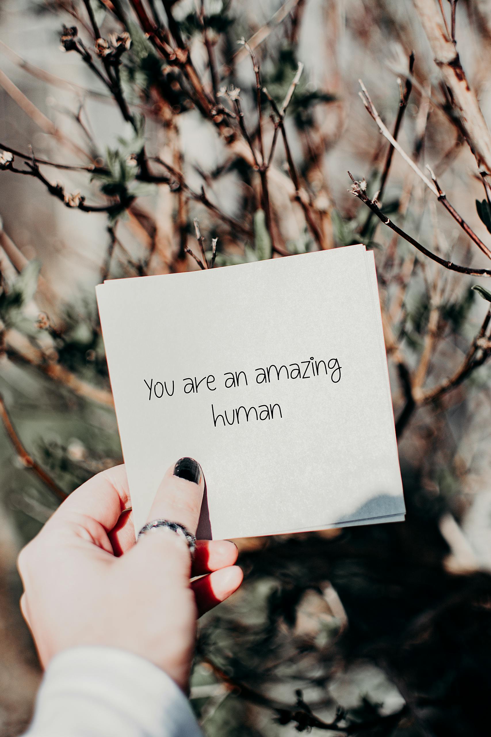Hand holding an inspirational quote card against a natural backdrop outdoors.
